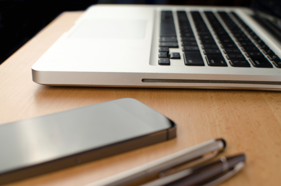 Ordinateur portable, téléphone et stylos sur un bureau en bois, poste de travail d'un indépendant