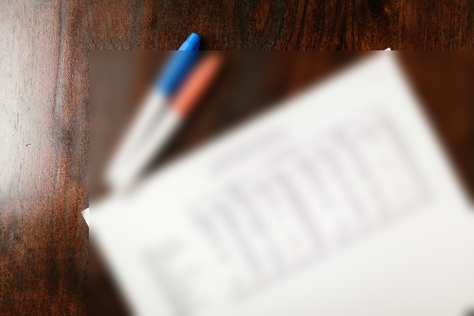 Bureau en bois avec deux stylos et un document chiffré volontairement flouté, évoquant le calcul de l'exonération LODEOM avec prime et treizième mois